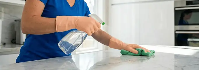 Maid service worker spraying and wiping a kitchen countertop with a microfiber cloth for sanitizing, Louisville, KY.