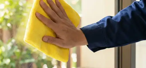 House cleaner wiping a glass window with a yellow microfiber cloth for streak-free cleaning, Louisville, KY.